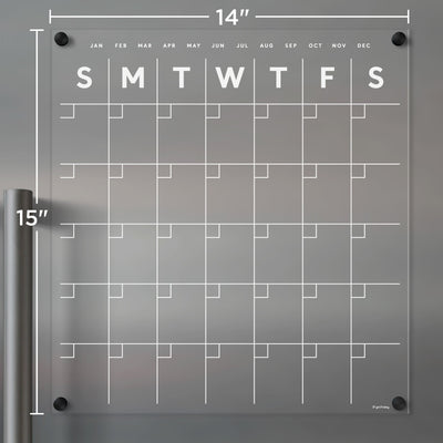 The Clear Acrylic Monthly Fridge Calendar by Girl Friday Shop, with white text, is a transparent 14x15-inch planning tool. Ideal with wet-erase markers, it features days and blank date squares, while months are elegantly listed along the top edge for easy reference.