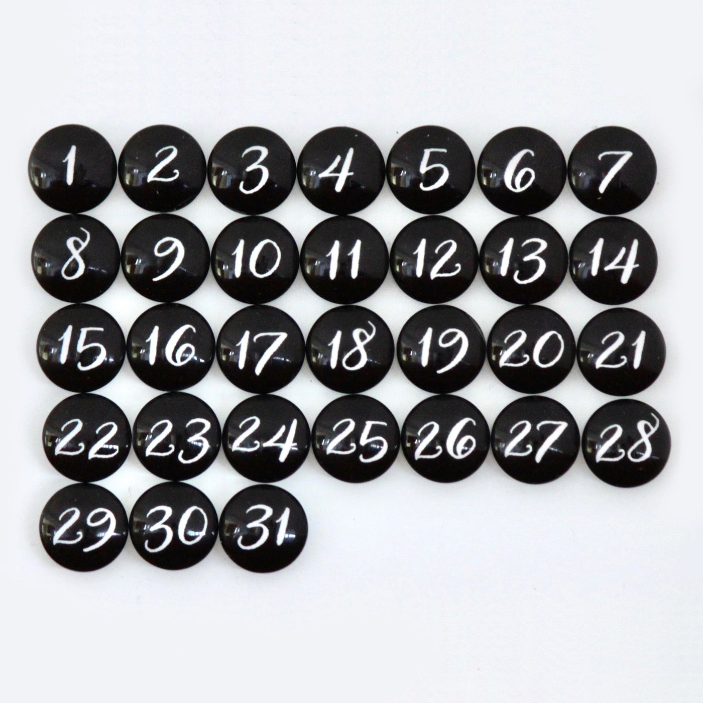 CalendarGirlCompanys #920 product features 31 black circular magnets resembling a chalkboard menu, each with white handwritten numbers from 1 to 31, arranged in rows on a clean white surface.