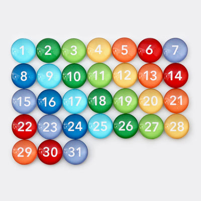 On a 9 X 24 framed weekly chalkboard calendar from CalendarGirlCompany, colorful round magnets numbered 1 to 31 create a gradient from blue to red and orange when arranged on the white surface.