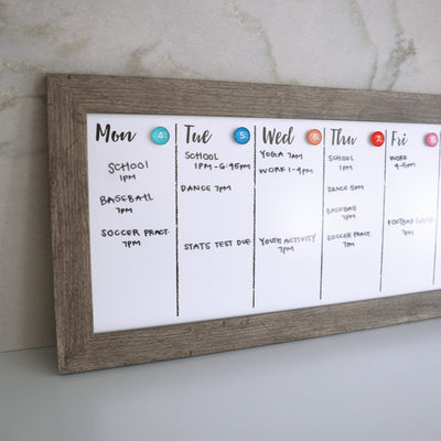 The CalendarGirlCompany 24 X 9 Framed Weekly Whiteboard Calendar (#922) features a premium acrylic surface for vibrant chalk ink markers. Display school, yoga, baseball, dance, and test schedules with colorful magnets in a wooden frame on a light wall for Monday through Friday.