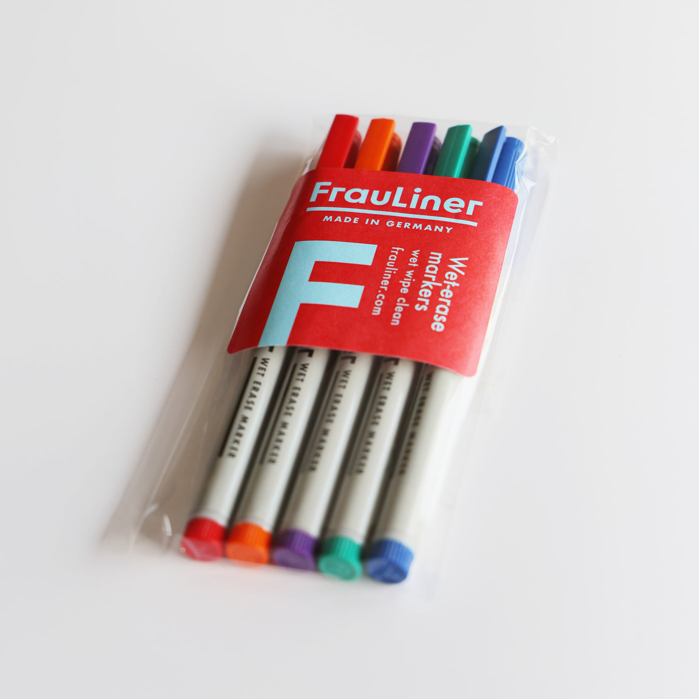 Set of six Girl Friday Shop FrauLiner fine tip wet-erase markers in a clear package. Non-toxic with colorful caps: orange, red, purple, green, blue, and black. Wrapped in a red label with FrauLiner and Made in Germany, perfect for acrylic boards.