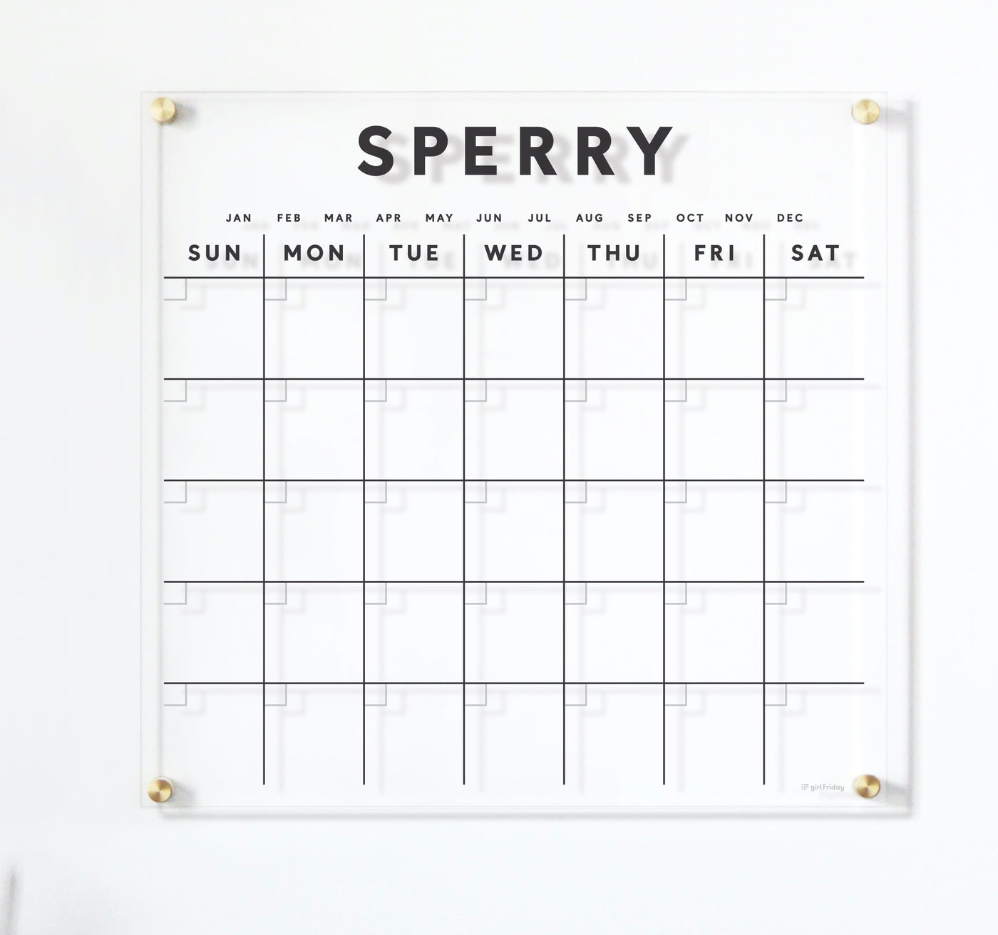 The Girl Friday Clear Acrylic Customizable Monthly Wall Calendar is a minimalist white calendar with a grid format displaying January to December and days Sunday to Saturday; Sperry is printed on top, and its compatible with wet-erase markers for easy updates.