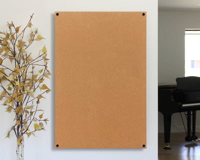 A Girl Friday Shop Modern Cork Board with custom cutting, mounted on a white wall with four visible screws, is complemented by a decorative autumn branch and a black grand piano in soft light, creating an inspiring and creative atmosphere.