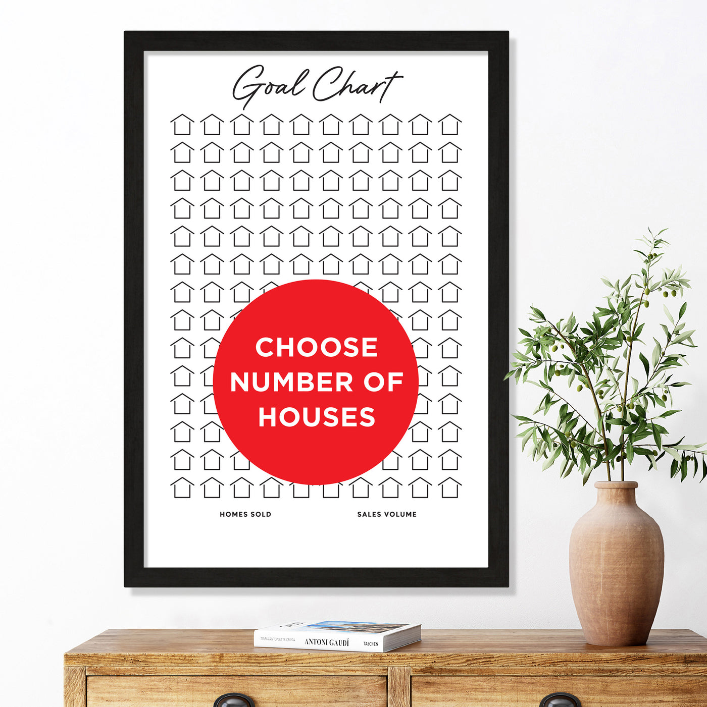 The Girl Friday Shops Goal Chart, a customizable real estate sales tracker with an empty house design, features a central red circle labeled Choose Number of Houses. Below, a vase with a small plant sits on a wooden cabinet.
