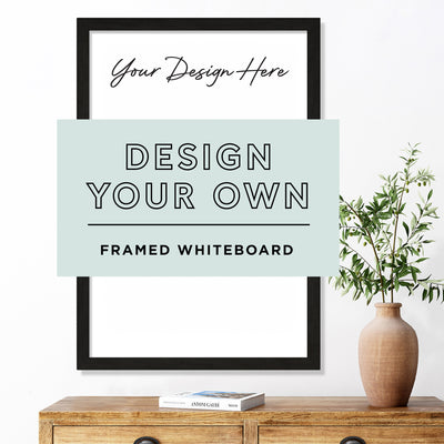 A Design Your Own Framed Acrylic Whiteboard | Vertical by Girl Friday Shop is displayed on a wooden surface. A potted plant sits to the right, and the words Design Your Own Framed Whiteboard appear on a pale green rectangle, inviting you to explore premium acrylic custom design options.