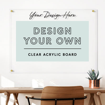 A contemporary workspace includes a wooden chair, desk with a plant, and the Girl Friday Shops Clear Acrylic Design Your Own Board in horizontal format above. Customize your board with wet-erase markers and add personal flair to your space.