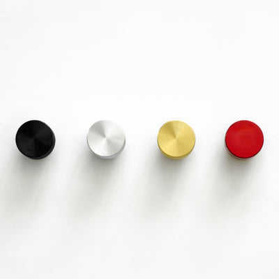 A set of four round metallic knobs in black, silver, gold, and red align horizontally on a white surface. Perfect for attaching to the Magnetic Chore Chart cover by Girl Friday Shop to create an organized and stylish chore chart.