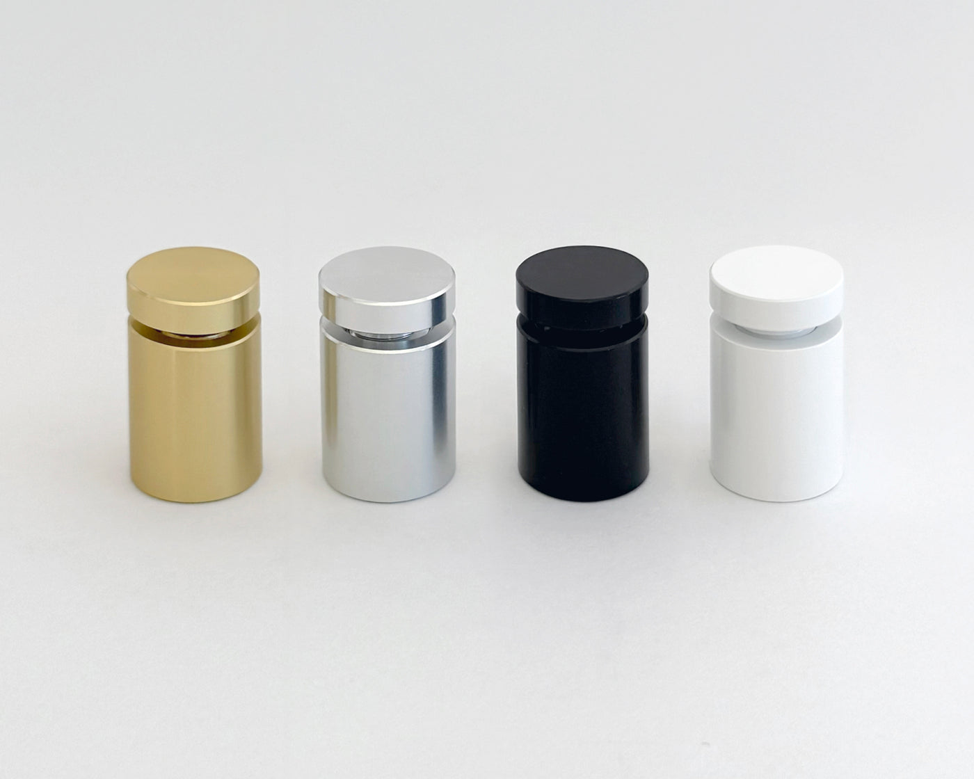 Four cylindrical bottles with caps, left to right in gold, silver, black, and white, gleam on a plain light gray surface. This arrangement mirrors the refined elegance typical of an Acrylic Art print designed by a talented Ukrainian artist from Girl Friday.