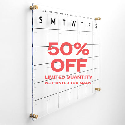 The Girl Friday Shops Clear Acrylic Monthly Wall Calendar, with a days grid from Sunday to Saturday, features bold black text: 50% OFF, LIMITED QUANTITY, and WE PRINTED TOO MANY! Ideal for wet-erase markers. Grab yours before theyre gone!.