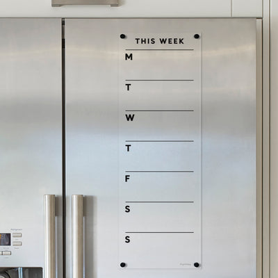 The Girl Friday Clear Acrylic Fridge Planner, with black text and a customizable title, mounts to your sleek silver refrigerator. It features daily columns under THIS WEEK for jotting notes with wet-erase markers, making it easy to update your menu board beside the fridge calendar.