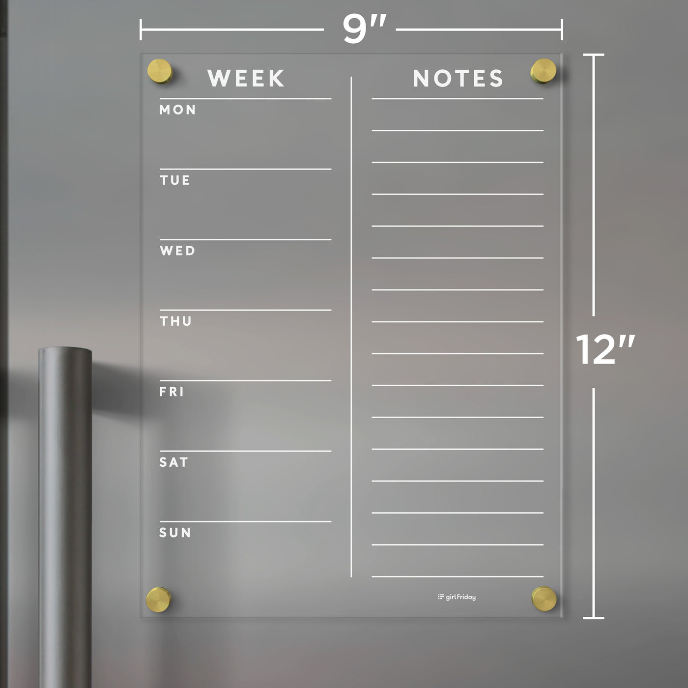 The Girl Friday Clear Acrylic Customizable Fridge Calendar, featuring gold corners and measuring 9x12 inches, is shown on a gray metal surface. It offers daily sections on the left and a notes area on the right, ideal for wet-erase markers.