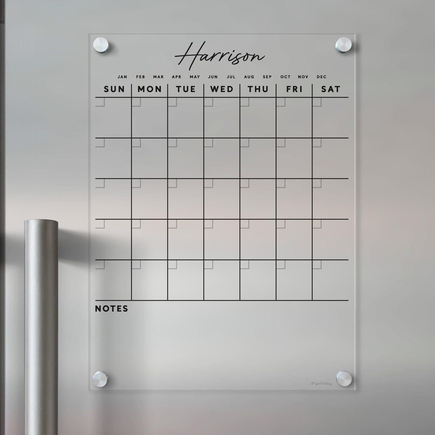 The Clear Acrylic Monthly Magnetic Fridge Calendar by Girl Friday features the name Harrison in script and includes a monthly grid with days of the week and notes section. Mounted on a light wall with four corner screws, it pairs well with wet-erase markers for easy updates.