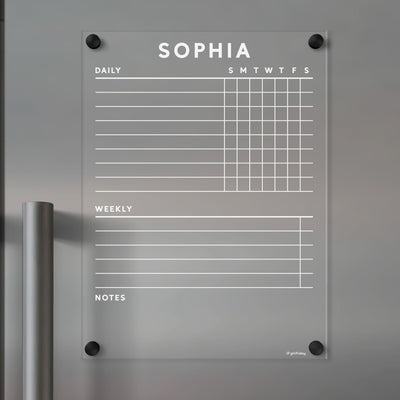 The Girl Friday acrylic fridge chore chart, featuring Sophia in white text, is perfect for organizing. It includes Daily, with a weekly grid, Weekly, and Notes sections. Mounted with black screws on a grey wall, it supports wet-erase markers for easy updates.