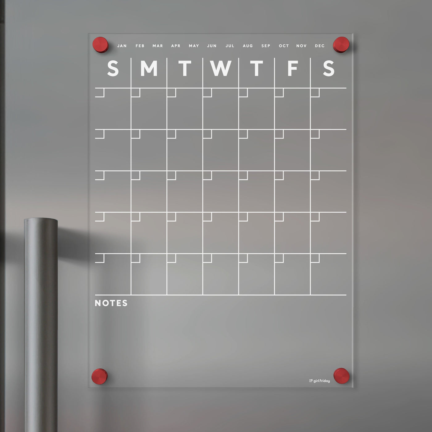 The Acrylic Fridge Calendar by Girl Friday features white text and a transparent acrylic design. Its wall-mounted with red pegs, ideal for dry-erase markers, displaying week days and months, with a NOTES section under the grid against a gray background.