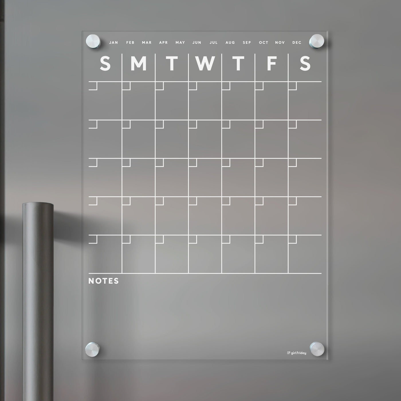 The Girl Friday Shops Clear Acrylic Monthly Fridge Calendar features a grid layout for days and months, with a bottom notes section. Its wall-mounted using visible screws and offers a modern, minimalist design. Use wet-erase markers for easy updates on this sleek surface.
