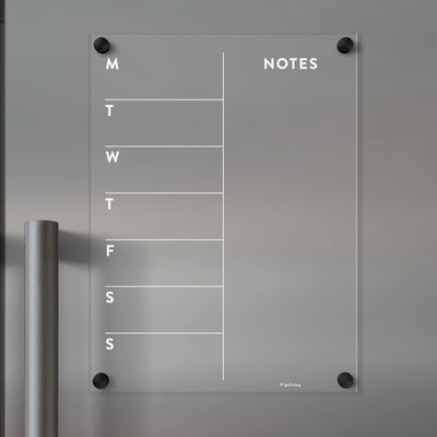 The Girl Friday Clear Acrylic Fridge Calendar is a glass weekly planner that mounts to the wall with black screws, featuring columns for each day of the week and a Notes section, ideal for wet-erase markers.