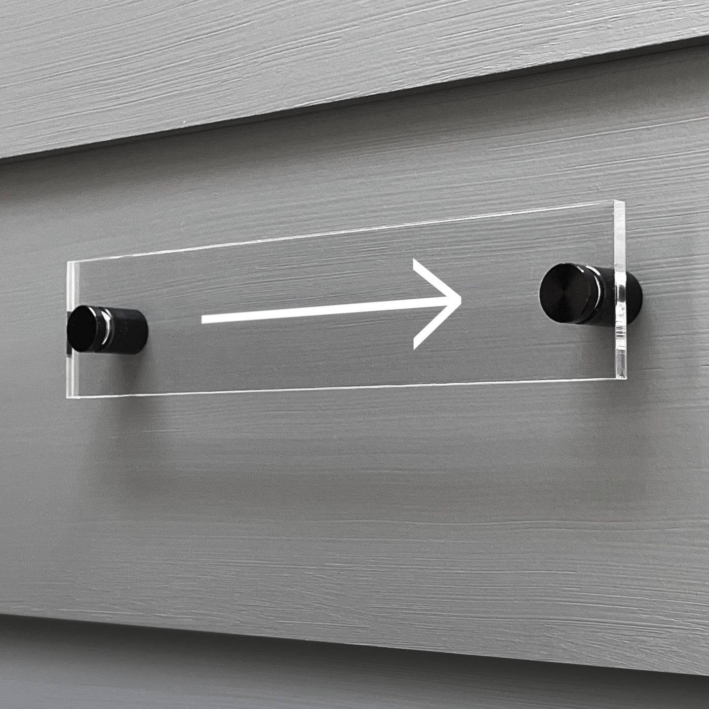 The Arrow Acrylic sign from Girl Friday Shop is custom mounted on a gray wall with black standoffs, showcasing a sleek white arrow pointing right.