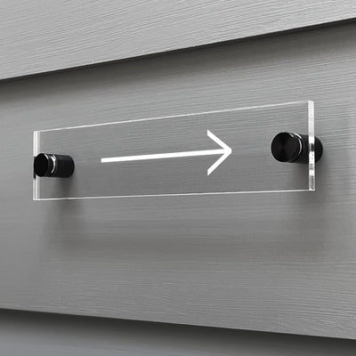 The Arrow Acrylic sign from Girl Friday Shop is custom mounted on a gray wall with black standoffs, showcasing a sleek white arrow pointing right.