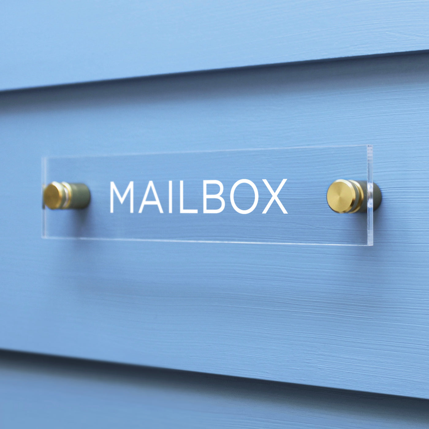 The Girl Friday Shop Mailbox Acrylic Sign features bold white capital letters on a clear surface, mounted on a light blue wall using two gold screws.