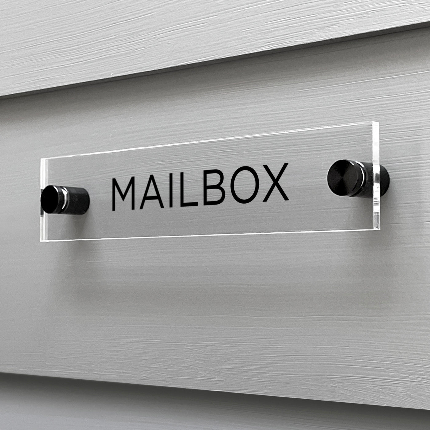 The Mailbox Acrylic Sign by Girl Friday Shop features a sleek design with bold black letters elegantly mounted on a gray wall using metal standoffs for a modern, custom look.