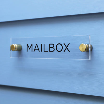 The Girl Friday Shop Mailbox Acrylic Sign features bold black MAILBOX lettering and mounts elegantly on a light blue wall with gold hardware.