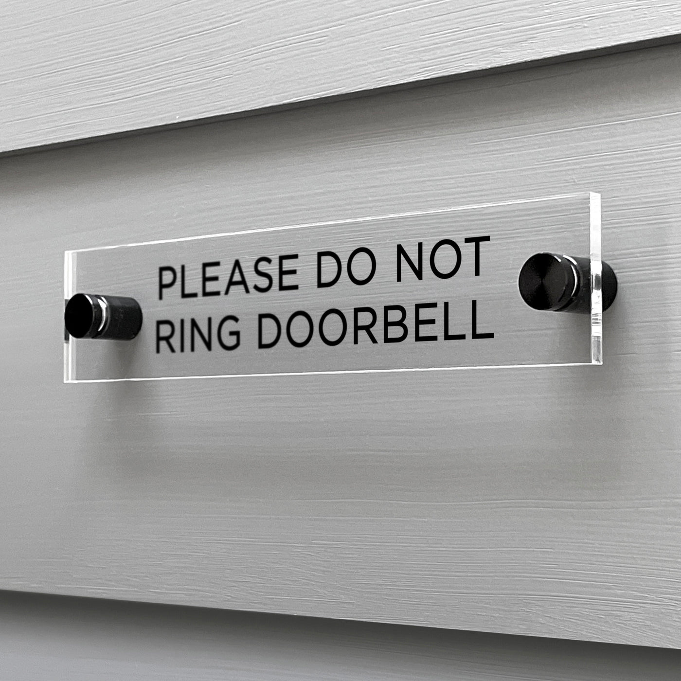 A sleek Girl Friday Shop acrylic sign, labeled Please Do Not Ring Door Bell in bold black letters, is securely mounted to the wall with two black screws.