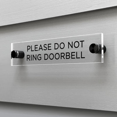 A sleek Girl Friday Shop acrylic sign, labeled Please Do Not Ring Door Bell in bold black letters, is securely mounted to the wall with two black screws.