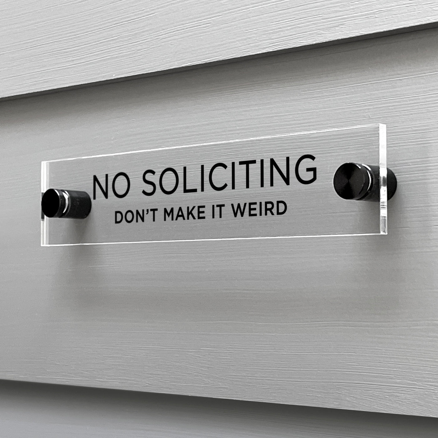 A No Soliciting Dont Make It Weird acrylic sign by Girl Friday Shop is mounted on a light gray wall. Boldly announcing NO SOLICITING with a playful DONT MAKE IT WEIRD in smaller font, its stylishly secured by two black mounts.