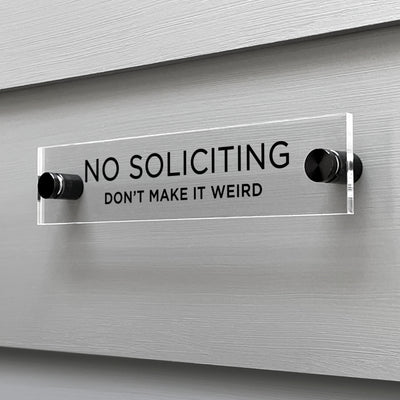 A No Soliciting Dont Make It Weird acrylic sign by Girl Friday Shop is mounted on a light gray wall. Boldly announcing NO SOLICITING with a playful DONT MAKE IT WEIRD in smaller font, its stylishly secured by two black mounts.
