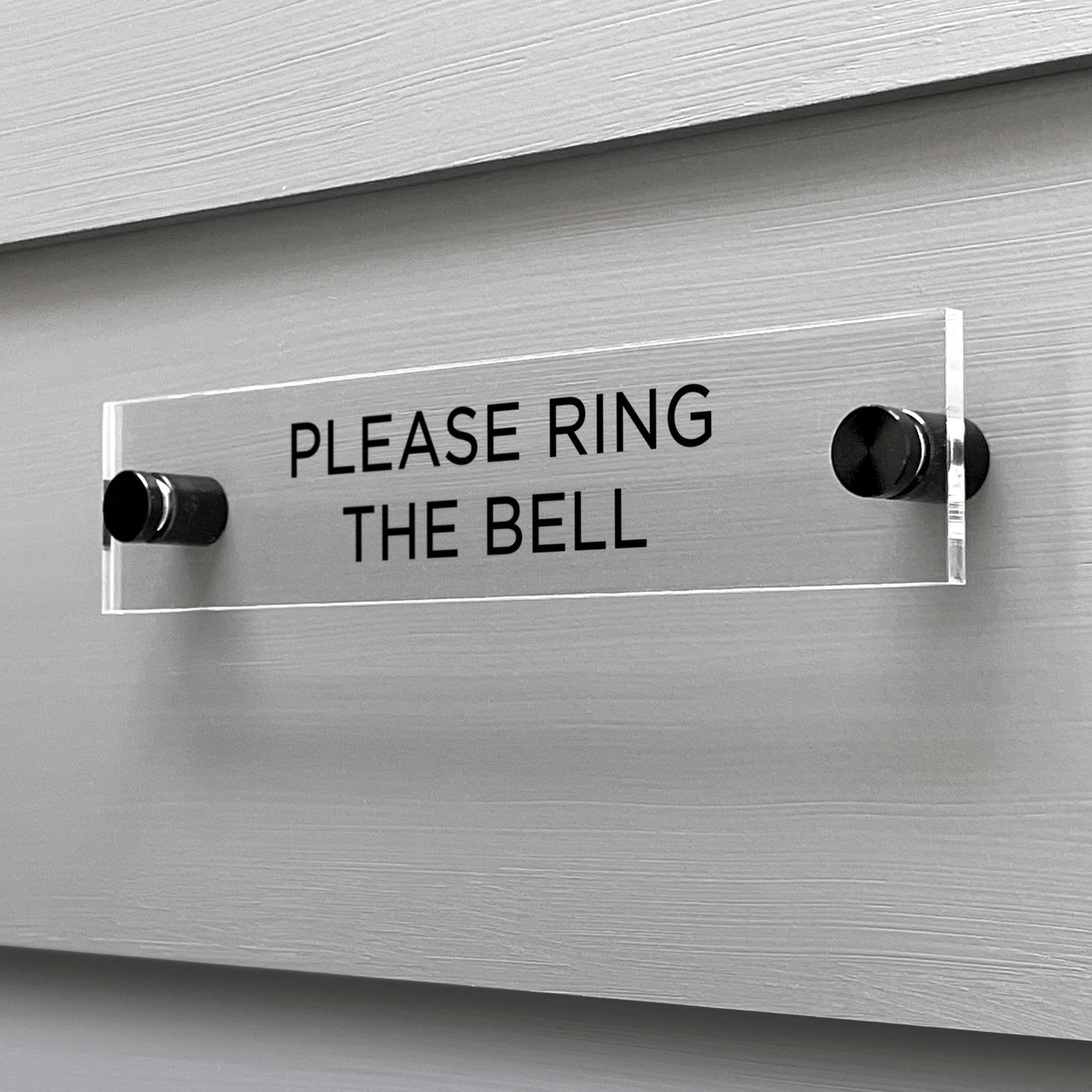 The Girl Friday Shops Please Ring The Bell acrylic sign, featuring black text, is elegantly mounted on a gray wall with metal standoffs.