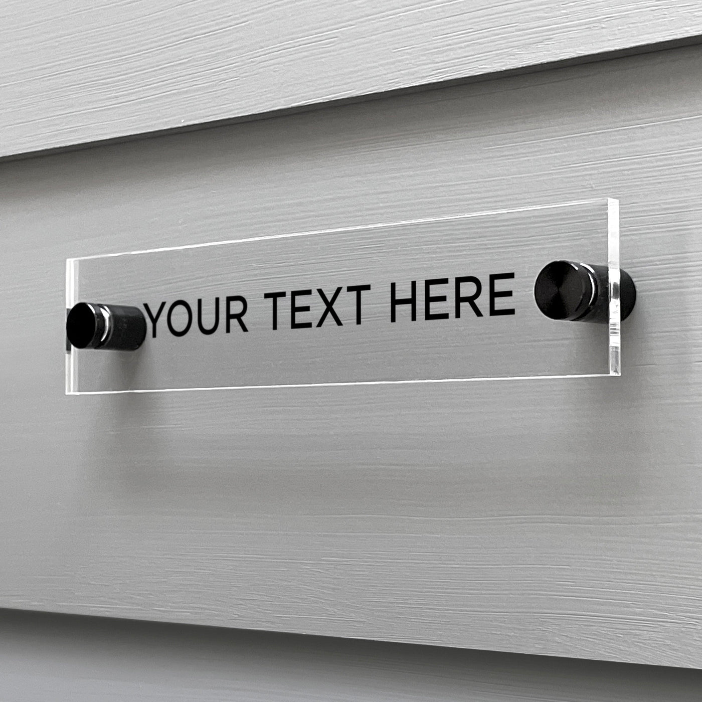 The Girl Friday Shops Design Your Own Acrylic Sign features bold black YOUR TEXT HERE text on clear American-made acrylic. Mounted with metal stand-offs for a floating effect, this piece on a gray wall invites custom text tailored to your vision.