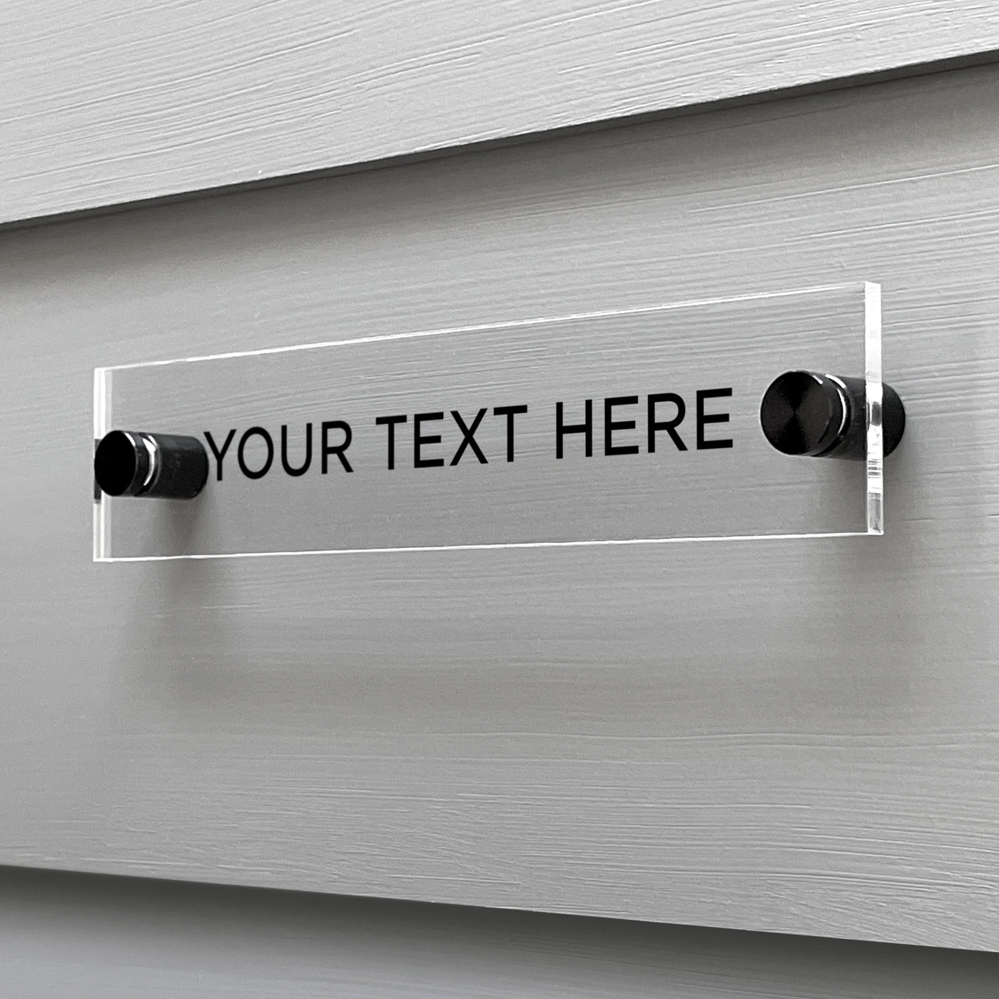 The Girl Friday Shops Your Text Here Acrylic Sign is affixed to a gray wall and features black placeholder text, offering an ideal canvas for customization.