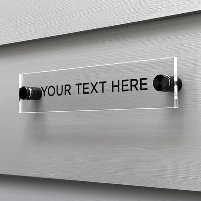 The Girl Friday Shops Your Text Here Acrylic Sign is affixed to a gray wall and features black placeholder text, offering an ideal canvas for customization.