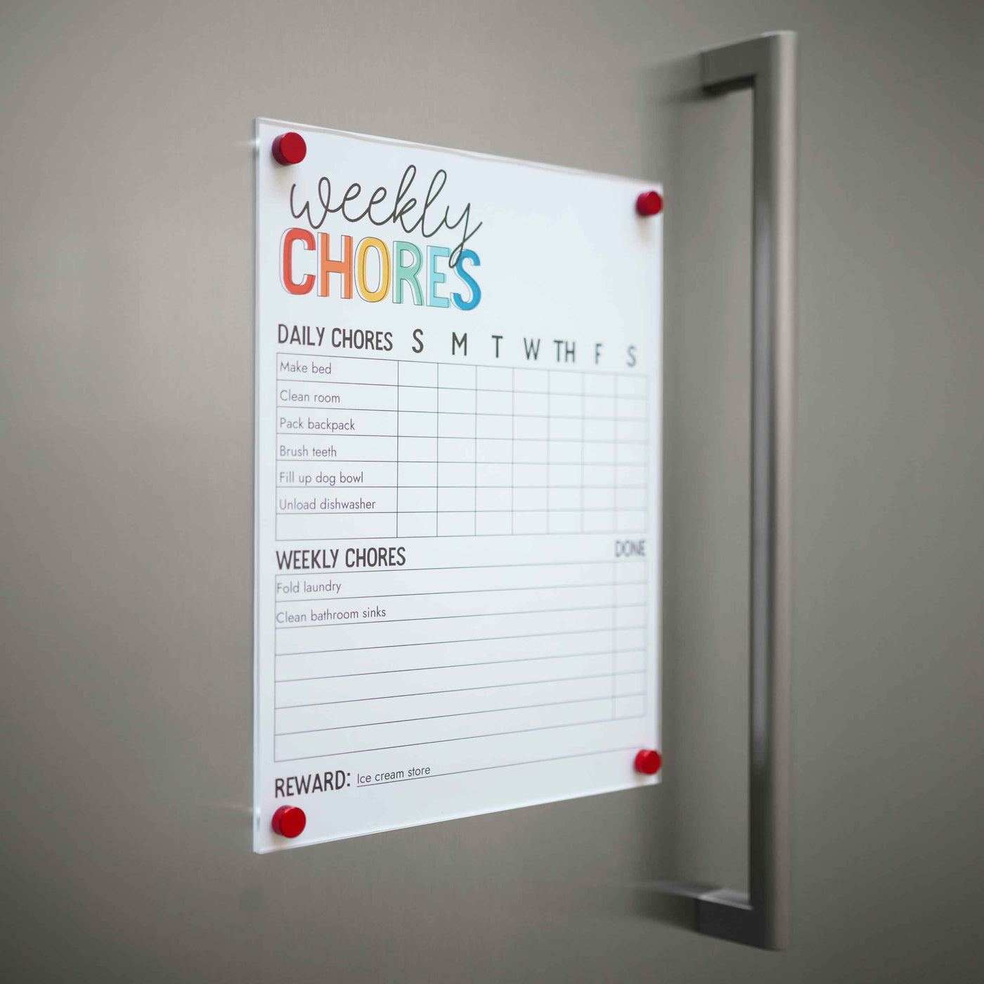 A Weekly Chores chart from Girl Friday Shop is pinned to a wall using their Magnetic Chore Chart Cover, listing daily tasks like bed-making and dishwashing, plus weekly chores such as laundry folding. Rewards include a trip to the ice cream store.