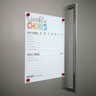 A Weekly Chores chart from Girl Friday Shop is pinned to a wall using their Magnetic Chore Chart Cover, listing daily tasks like bed-making and dishwashing, plus weekly chores such as laundry folding. Rewards include a trip to the ice cream store.