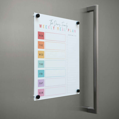 A weekly meal plan clings to the metallic fridge, featuring a Girl Friday Shop Magnetic Chore Chart cover. Its magnetic dry erase labels mark each day for easy reuse, transforming menu planning into an effortless chore chart with vibrant organization.