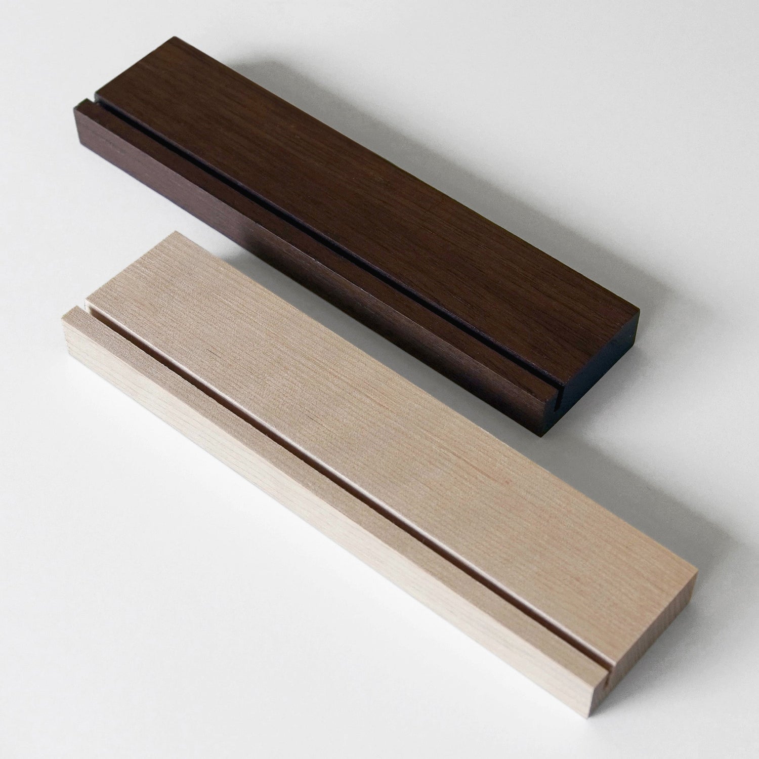 The Girl Friday Weekly Black Acrylic Calendar with Wood Stand features two rectangular wooden blocks in dark brown and light beige, each with a narrow groove. Theyre perfect for organizing your desk or calendar notes with style on a white surface.