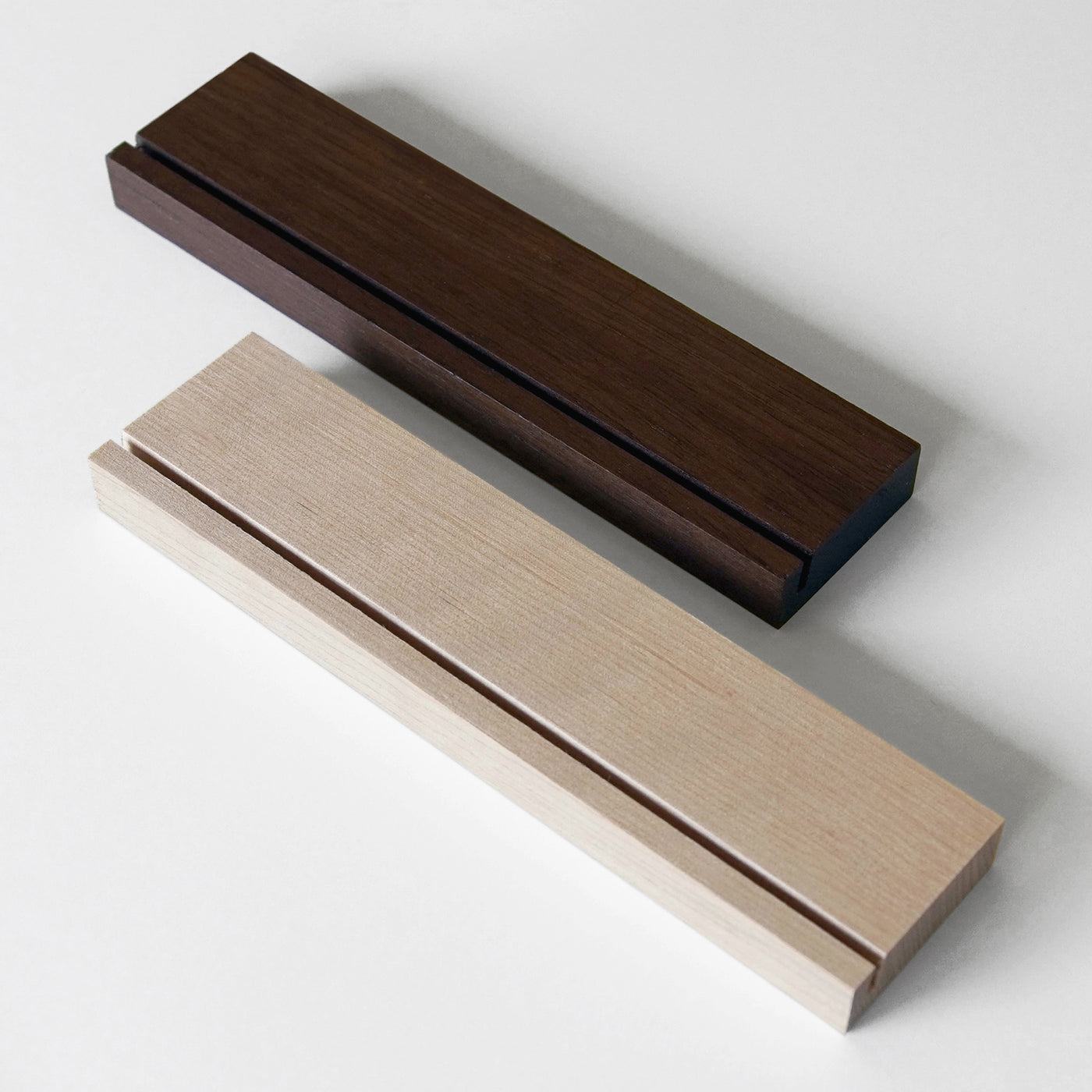 The Girl Friday Weekly Black Acrylic Calendar with Wood Stand features two rectangular wooden blocks in dark brown and light beige, each with a narrow groove. Theyre perfect for organizing your desk or calendar notes with style on a white surface.