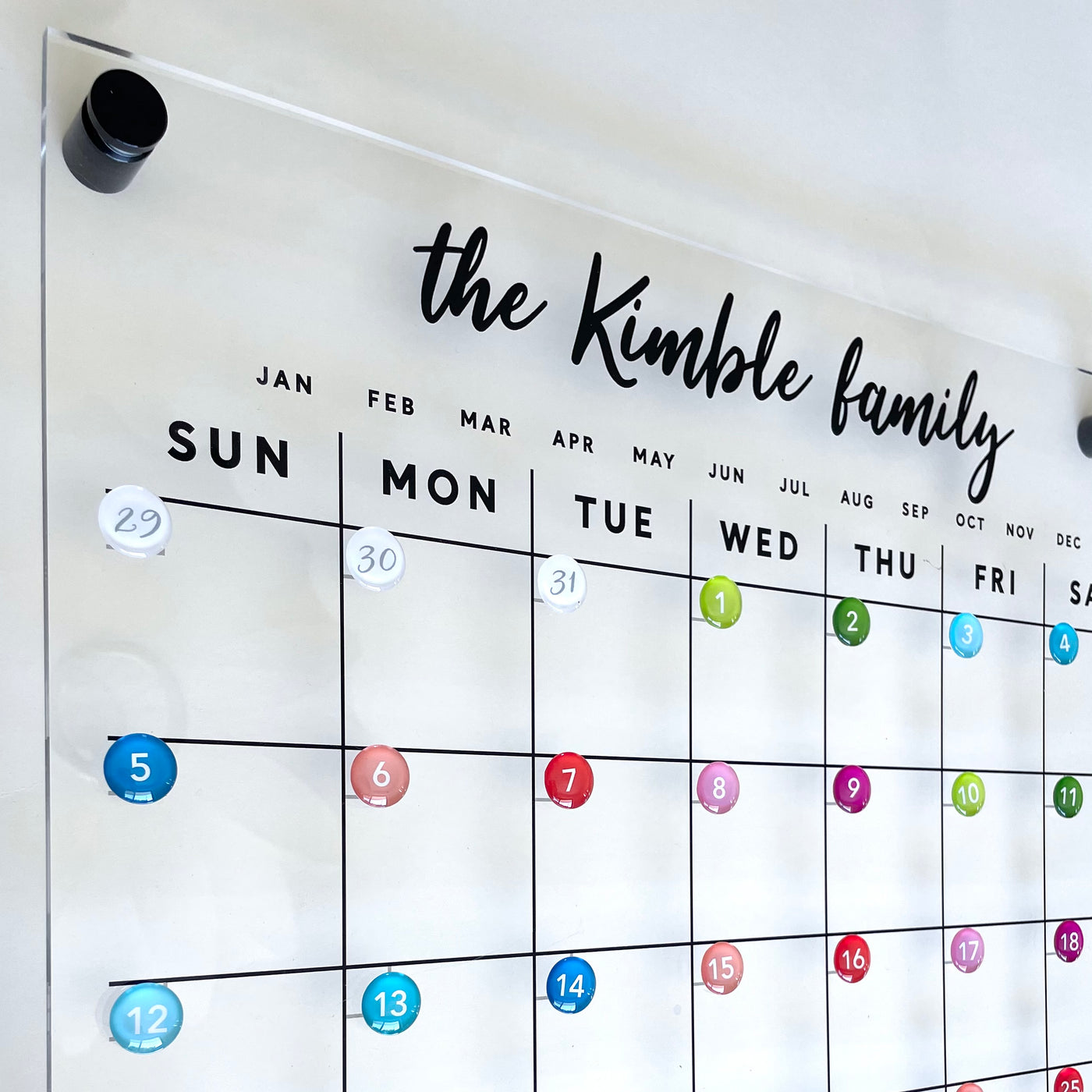 The Kimble family calendar, designed by Girl Friday, is a vibrant magnetic grid with months and days. It features colored circle magnets for appointments, with dates 29, 30, and 31 prominently in the upper left corner using Metal disks for clear viewing.