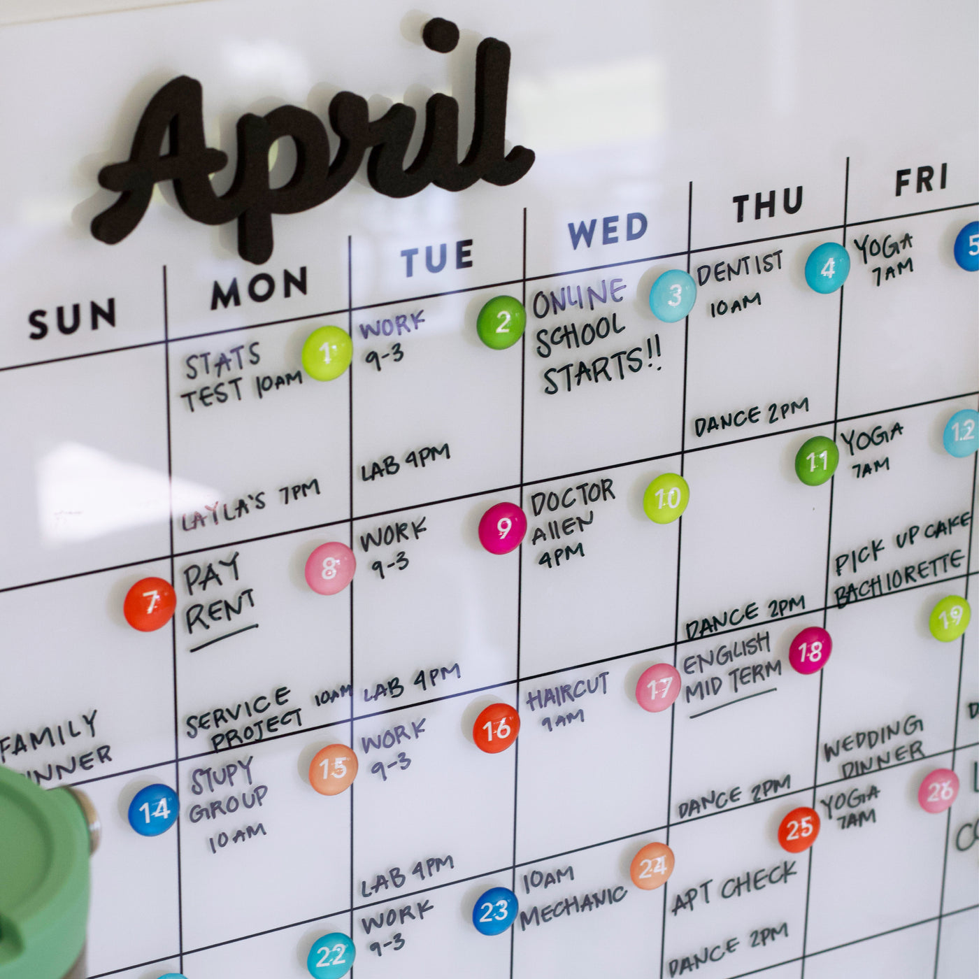 The Girl Friday Shops White Acrylic Monthly Calendar for April offers a sleek dry erase surface for vibrant markers and magnets or command strip mounting to securely display packed schedules, like tests, work shifts, online school starts, appointments, and dance sessions.