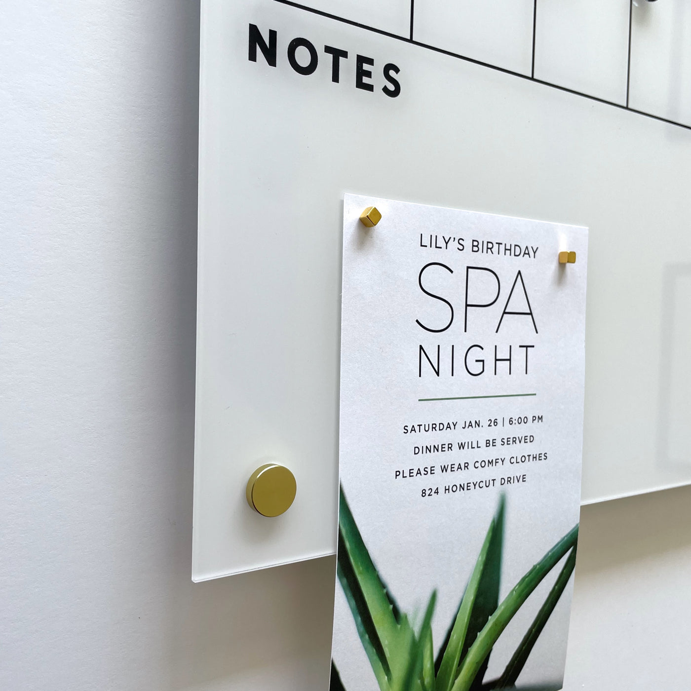 A whiteboard with NOTES at the top features a paper detailing Lilys birthday Spa Night, set for Saturday, Jan 28, 6:00 PM, at 824 Honeycut Drive. The paper is secured with stylish Gold Strong Magnets by Girl Friday Shop.