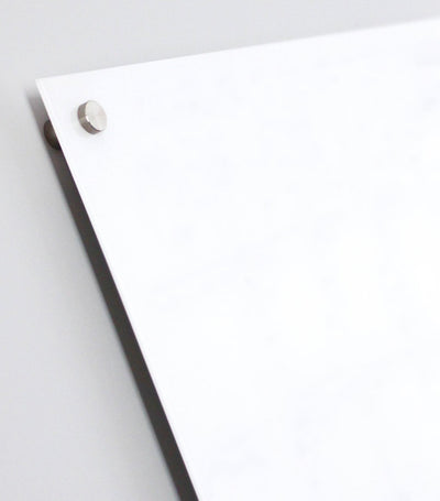 Close-up of a corner of the Design Your Own Floating White Acrylic Board | Horizontal by Girl Friday, mounted with metal standoffs. The premium dry erase surface on a neutral light gray background transforms spaces into customizable whiteboards.