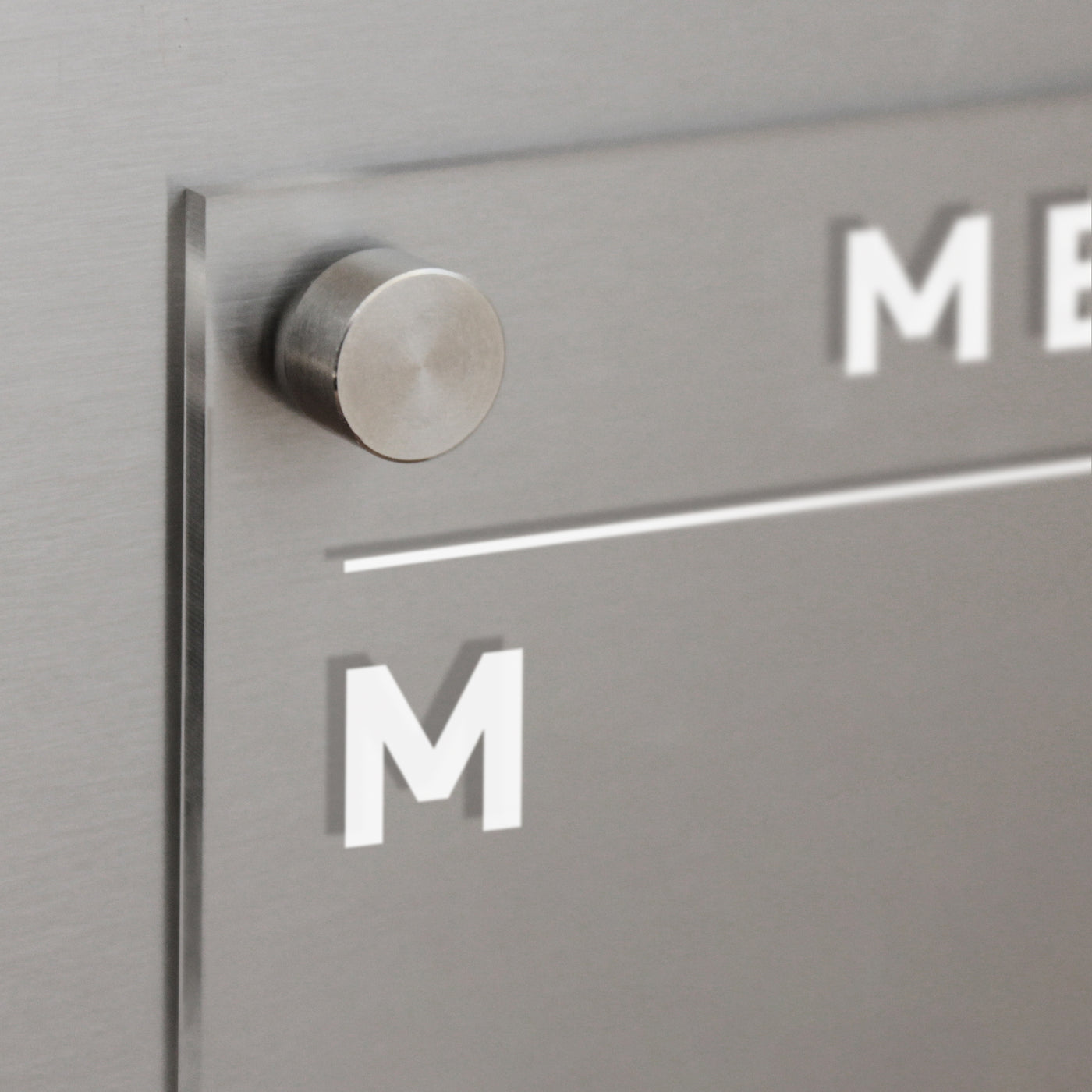 A sleek, brushed metal sign with a glass panel and cylindrical spacer evokes the style of Girl Fridays Clear Acrylic Fridge Calendar Menu Board. The white M and ME resemble organized days planned with wet-erase markers.