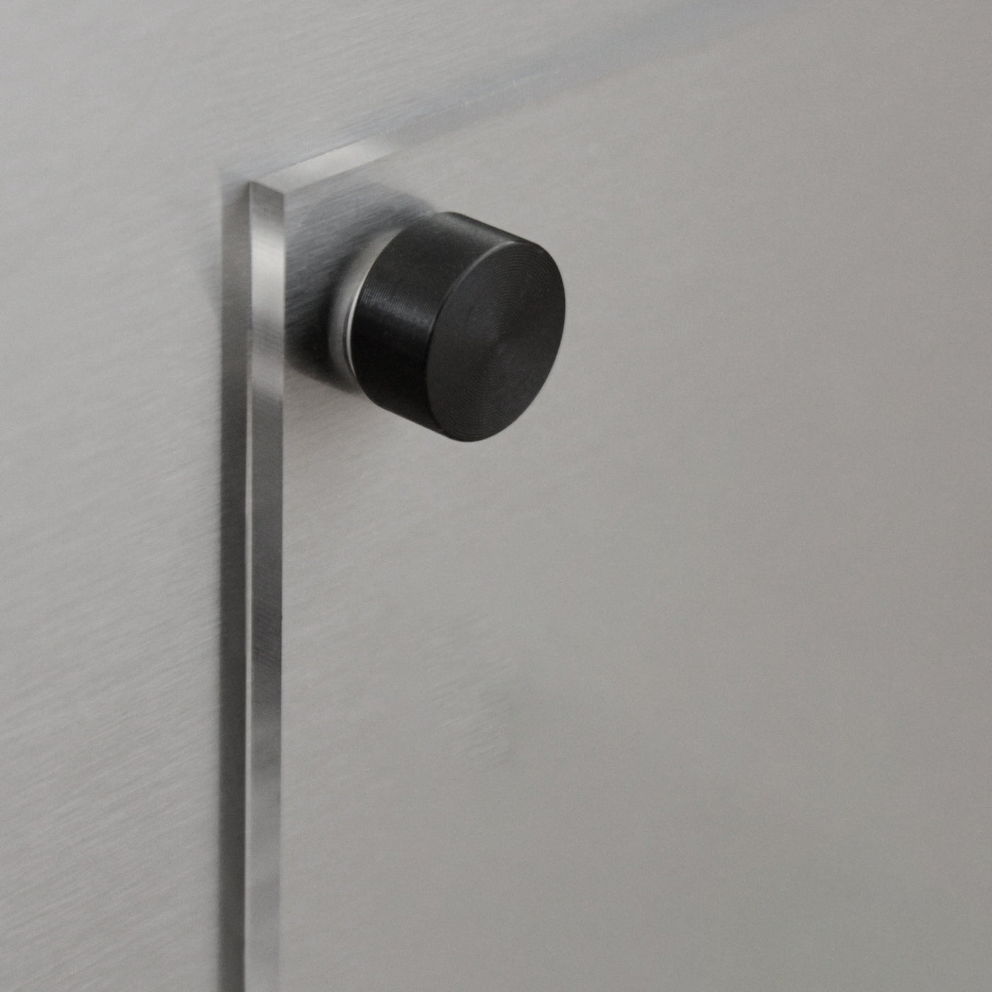A close-up shows a brushed metal surface featuring a round, black knob that casts a shadow. Ideal for securing the Girl Friday Shop’s Clear Acrylic Fridge Meal Planner, it emphasizes the smooth, matte texture of the metallic background.