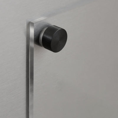A close-up shows a brushed metal surface featuring a round, black knob that casts a shadow. Ideal for securing the Girl Friday Shop’s Clear Acrylic Fridge Meal Planner, it emphasizes the smooth, matte texture of the metallic background.