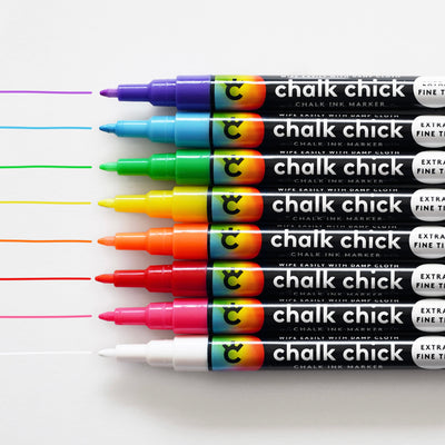 Eight vibrant Chalk Chick markers are neatly arranged horizontally, with colored lines extending from each tip. Ideal for an 18 x 24 Framed Chalkboard Calendar by CalendarGirlCompany, these come in purple, blue, green, yellow, orange, red, pink, and white.