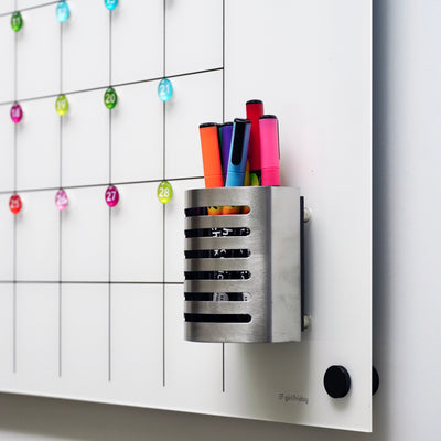 The Girl Friday wall-mounted magnetic acrylic calendar includes a Magnetic Stainless Steel Marker holder, colorful markers, and numbered circles for each day. Powerful black circular magnets keep notes secure on the integrated whiteboard.