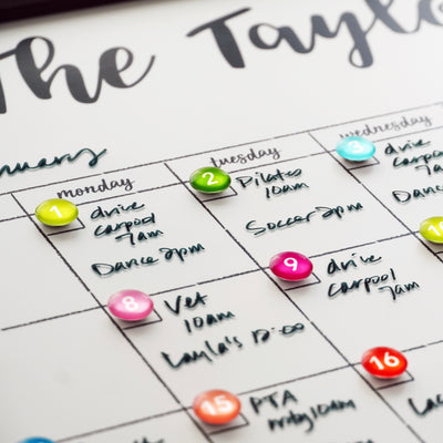 A 24 X 18 framed whiteboard calendar by CalendarGirlCompany (#18203) shows January filled with Pilates, soccer, dance, a vet appointment, and other personal engagements creatively written in premium acrylic style using colorful pins and chalk ink markers.