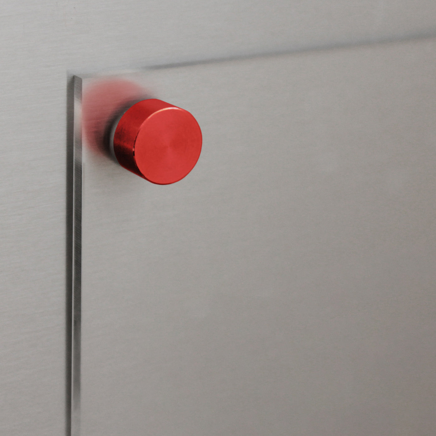 A close-up of a modern cabinet with a centrally attached red cylindrical knob contrasts against a sleek metallic surface, neatly holding the Clear Acrylic Fridge Meal Planner by Girl Friday Shop, creating a minimalist and contemporary design.