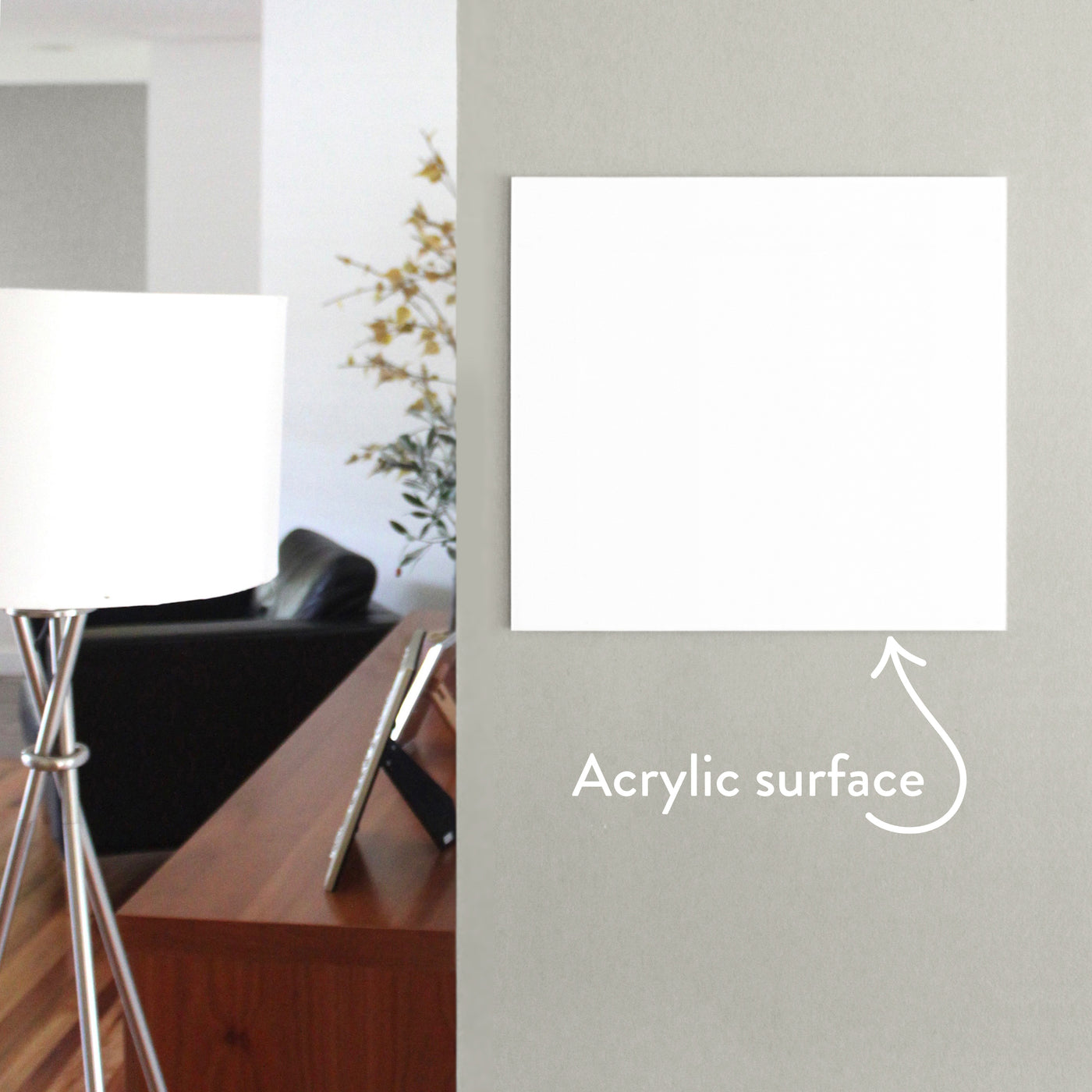 A modern room with minimalist design showcases a Girl Friday Shop White Acrylic Dry Erase Memo Board on a gray wall, labeled with an arrow. A sleek floor lamp with a white shade stands near the board, while a wooden table holding a photo frame contributes warmth to the scene.